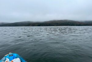 The tip of my kayak rests on the grey water of Tomales Bay with the fog-covered hills of Point Reyes Peninsula in the distance
