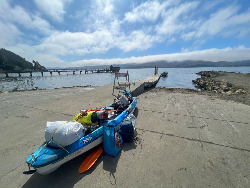 A long blue Pelican Kayak loaded with camping gear sits on the dock at Miller Boat Launch on Tomales Bay